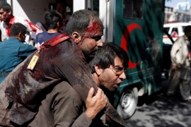 An Afghan man carries an injured man to a hospital after a blast in Kabul, Afghanistan