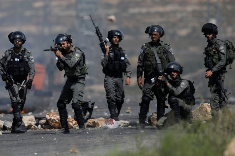 An Israeli border policeman aims his weapon at Palestinian protesters during clashes at a protest in support of Palestinian prisoners on hunger strike in Israeli jail, near Ramallah
