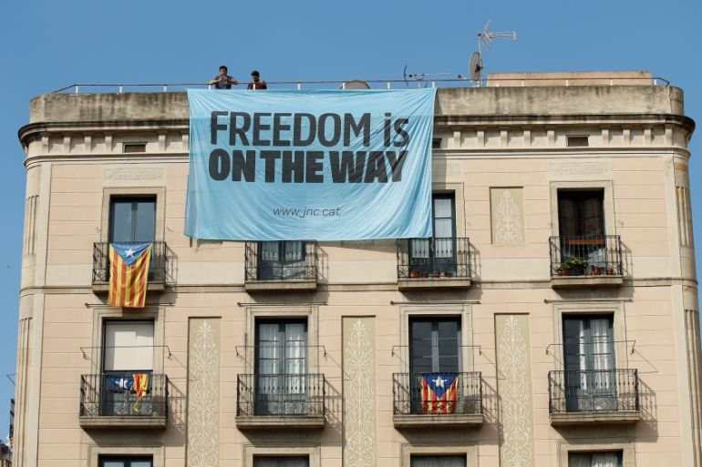 Catalonia independence supporters unfurl a banner on a building next to the Palau de la Generalitat, the regional government headquarters, in Barcelona