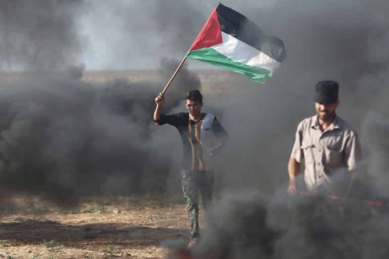 A protester holds a Palestinian flag during clashes with Israeli troops at a protest against reducing power supply to Gaza, near the border with Israel in Khan Younis in the southern Gaza Strip