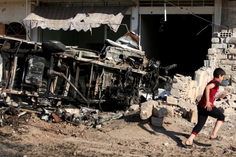 A boy walks past a damaged vehicle at a site hit by an airstrike in the rebel-held Tafas town