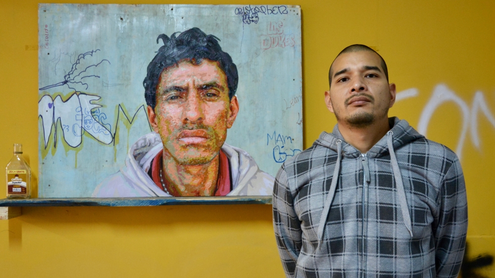 Aaron Lopez poses with one of his paintings. He seeks out his subjects - sicarios (hired hitmen) and drug traffickers - in the barrios, before photographing them, often on his mobile phone, and then painting their portraits [Paula Dupraz-Dobias/Al Jazeera]