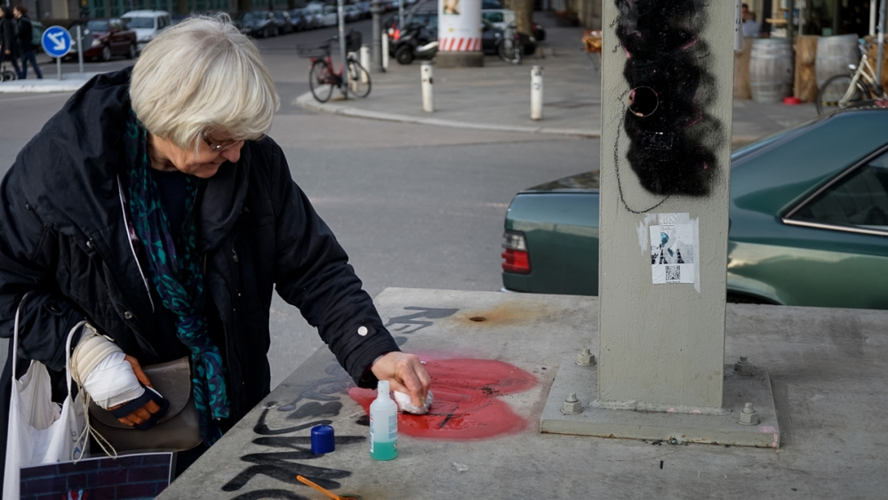 Mensah-Schramm uses nail polish remover to erase anti-refugee graffiti [Patrick Strickland/Al Jazeera]