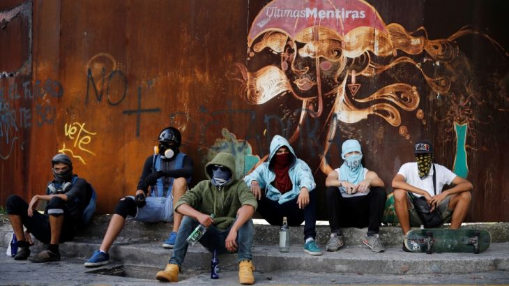 Protesters sit underneath a graffiti during a rally against Venezuela''s President Maduro''s government in Caracas