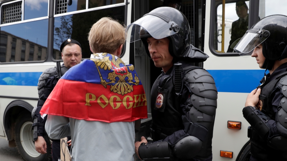 Riot police detain a man covered with Russian national flag in central Moscow [Tatyana Makeyeva/Reuters]