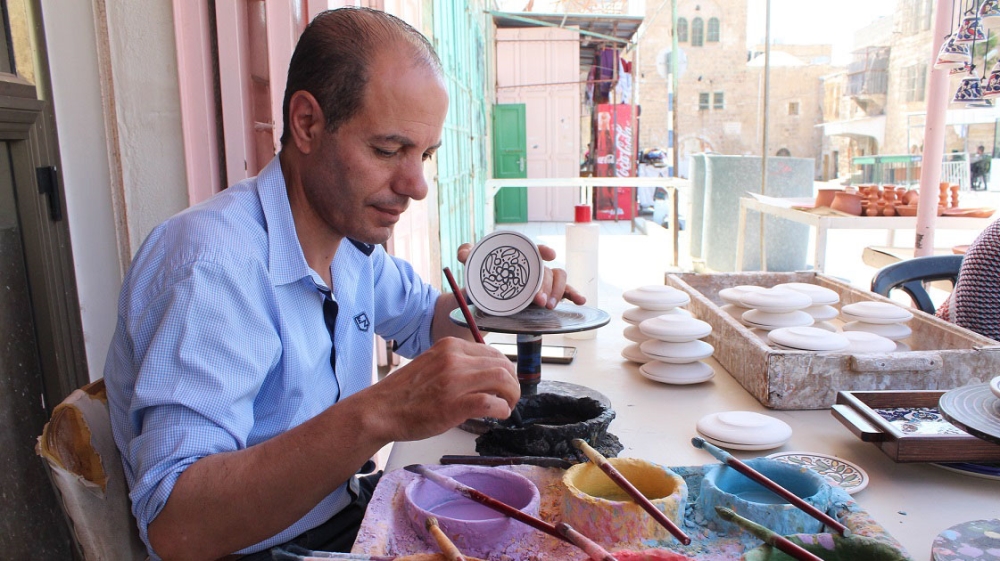 Khaled Mohammed paints a ceramic dish at his family's pottery workshop in Hebron's Old City [Nigel Wilson/Al Jazeera]