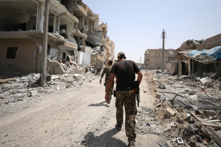 Fighters from Syrian Democratic Force (SDF) walk past damaged buildings in Raqqa city