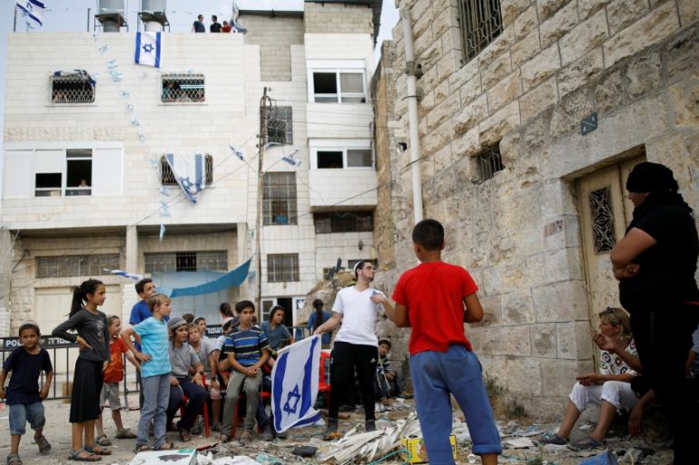 Jewish settler youth argue with Palestinian youth as a disputed building where about a hundred hard-line Jewish settlers have hunkered down is seen in the background, in the West Bank city of Hebron