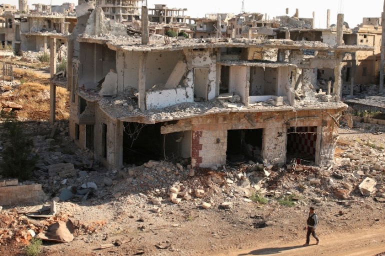 A rebel fighter walks past damaged buildings in a rebel-held part of the southern city of Deraa