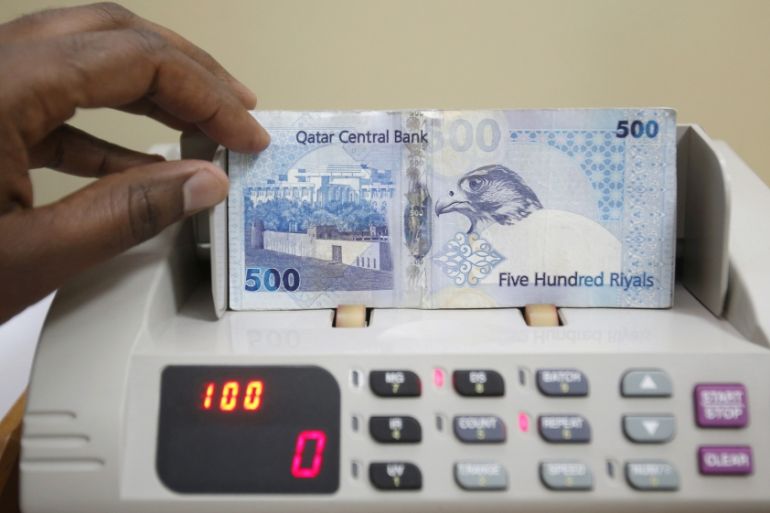 A cashier counts Qatari riyal notes at a money changer in Doha