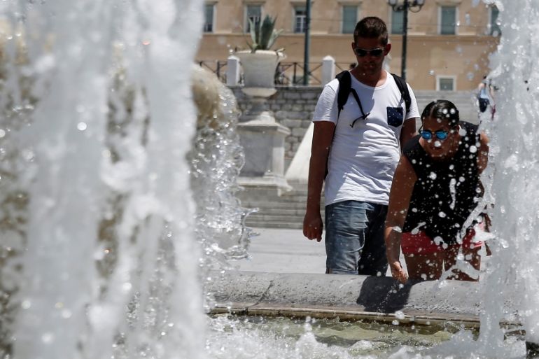 People cool off in a fountain of water during a hot Summer day in Athens