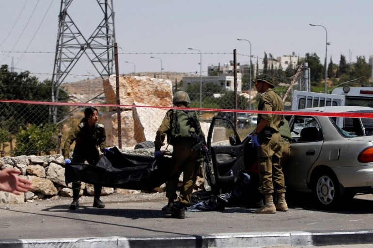 Israeli soldiers remove the dead body of a Palestinian assailant at the scene of a car-ramming attack at the entrance of Beit Einun village, near the West Bank City of Hebron