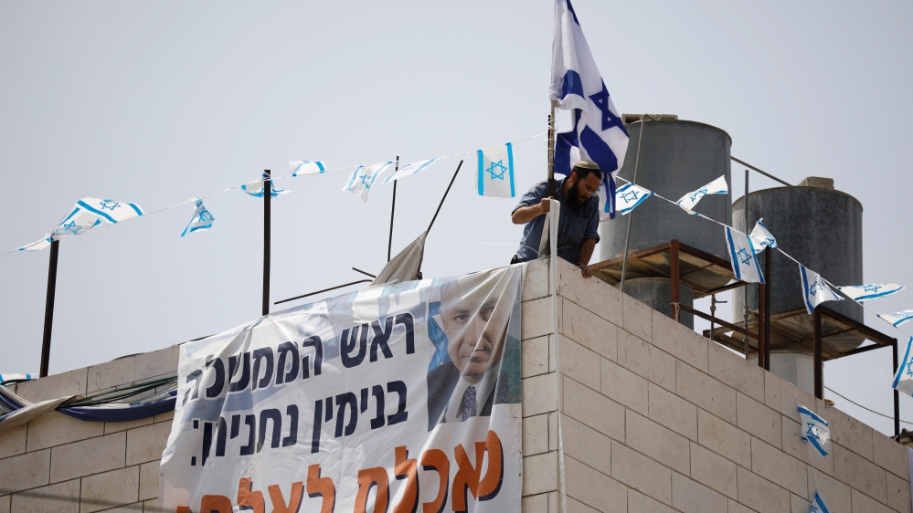 An Israeli settler hangs a banner calling on PM Netanyahu to allow them to stay in the home [Amir Cohen/Reuters]