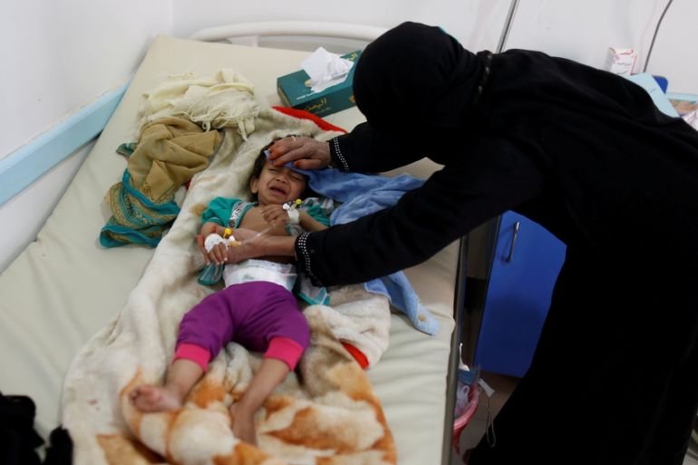 Woman helps her son as he lies on a bed at a cholera treatment center in Sanaa, Yemen