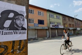 A man rides his bicycle past a poster of Burhan Wani, a commander of the Hizbul Mujahideen militant group, during restrictions on the occasion of Wani''s death anniversary, in Srinagar
