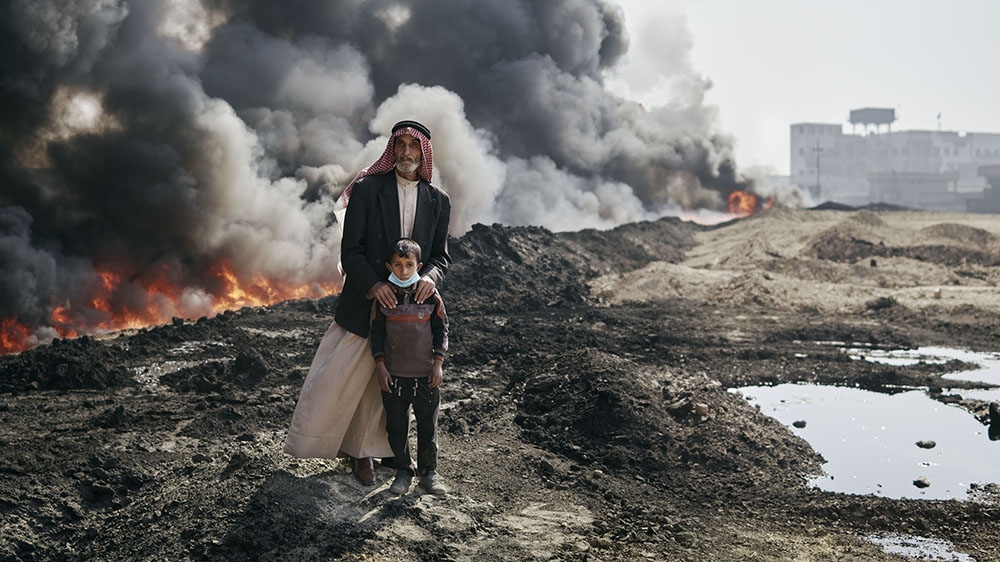 A village elder and a young boy pose for a portrait near one of the Qayyara infernos [Joey Lawrence/ Al Jazeera]