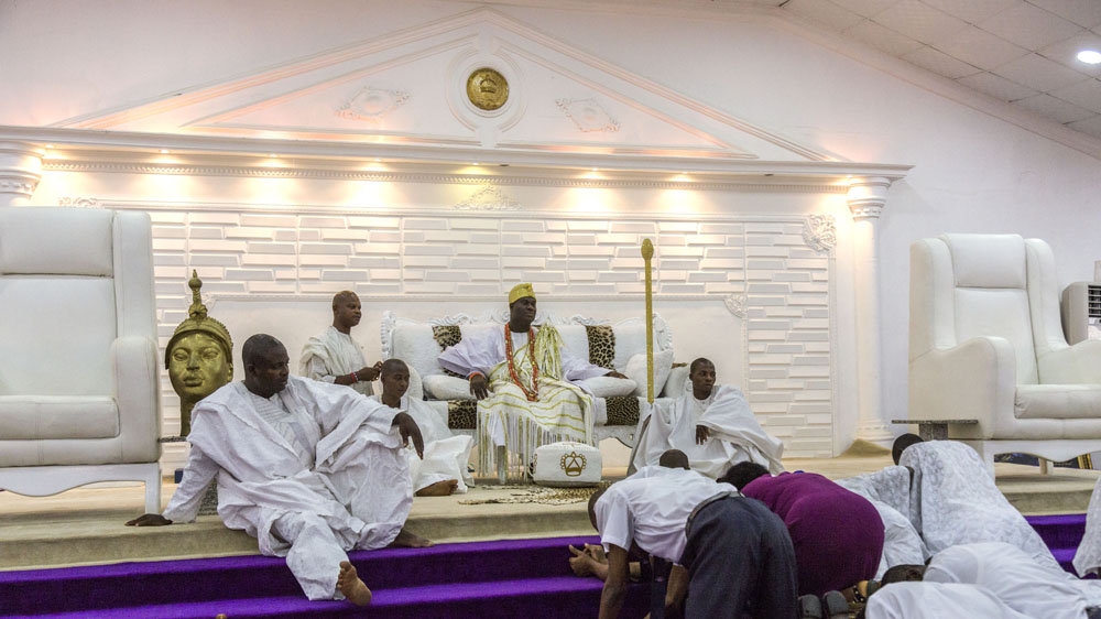 
Surrounded by his attendants, the Ooni receives guests, who must remain physically below him at all times and are only permitted to shake his hand if he initiates the contact [Andrew Esiebo/Al Jazeera]
