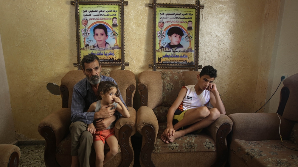 Muntaser sits with his father and sister, with photos of his slain brother and nephew hanging in the background [Ezz Zanoun/Al Jazeera]