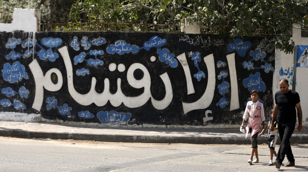 A Palestinian man and children walk past graffiti reading 