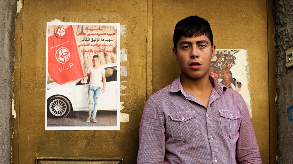 Ramzi standing beside a poster of slain Palestinian youngster Raed al-Salhi [Jaclynn Ashly/Al Jazeera]