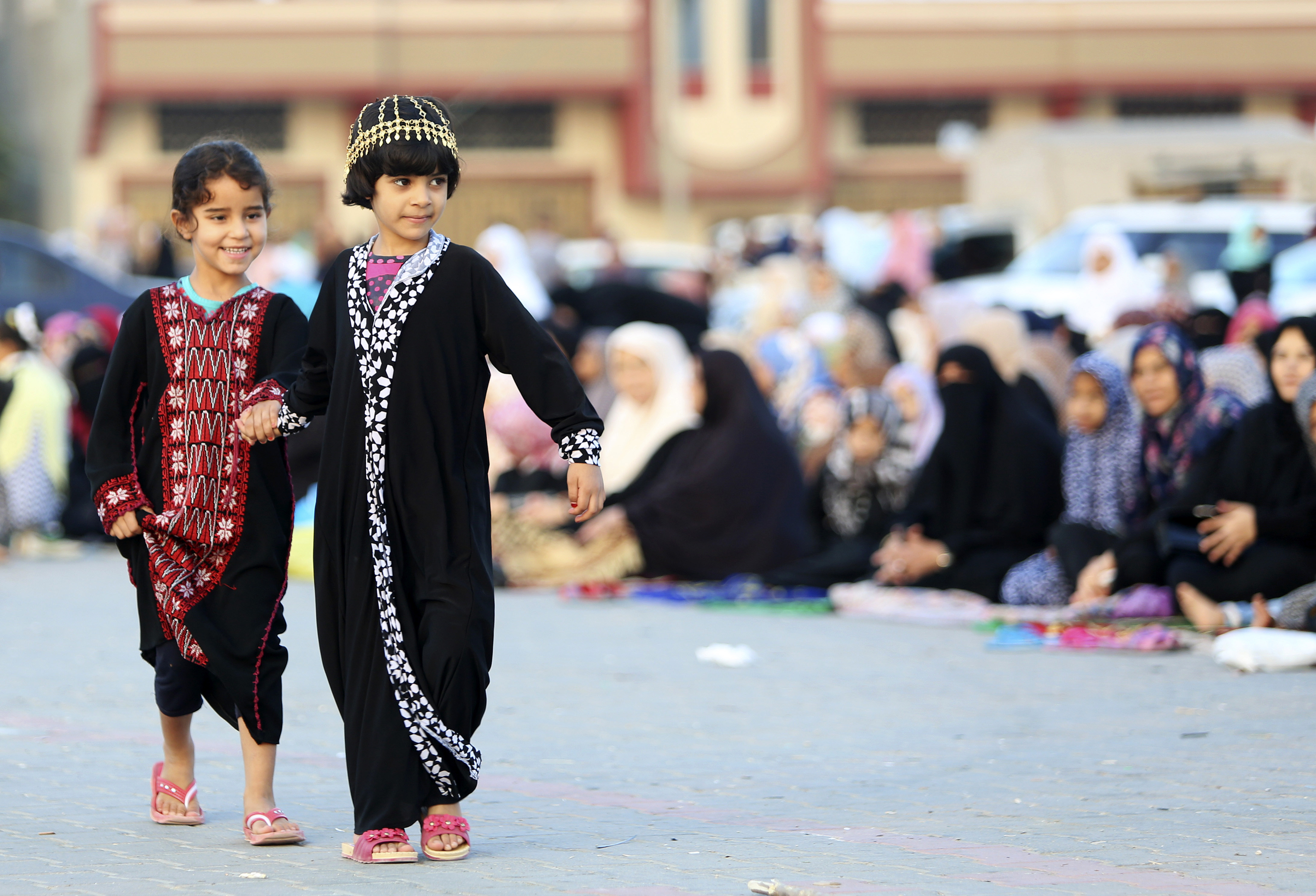 Girls walk in front of adults gathered to pray in Nusseirat refugee camp, central Gaza Strip [Adel Hana/AP]