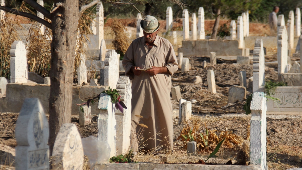 A Syrian man reads the Quran while visiting the graves of loved ones on the morning of the first day of Eid al-Adha [Omar Haj Kadour/AFP]