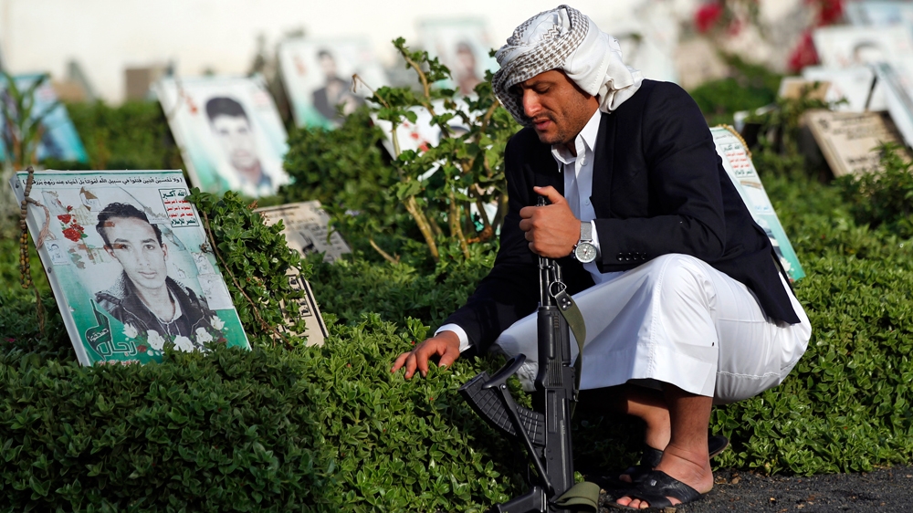 A Yemeni man holding a Kalashnikov assault rifle sits next to the grave of a loved one in a cemetery in the capital Sanaa [Mohammed Huwais/AFP]