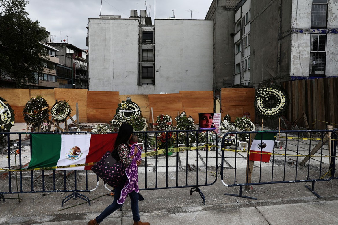 A resident holds her baby as they walk past a tribute to the victims at the site of a building that collapsed in Narvarte neighbourhood. REUTERS/Nacho Doce