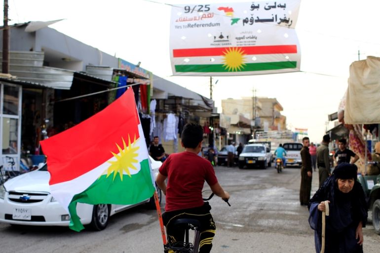 A boy rides a bicycle with the flag of Kurdistan in Tuz Khurmato