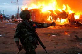 A riot policeman gestures near properties set on fire by rioters in Kawangware slums in Nairobi