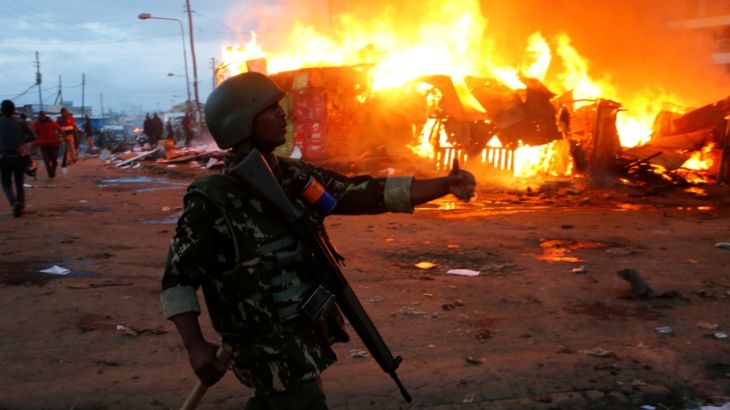 A riot policeman gestures near properties set on fire by rioters in Kawangware slums in Nairobi