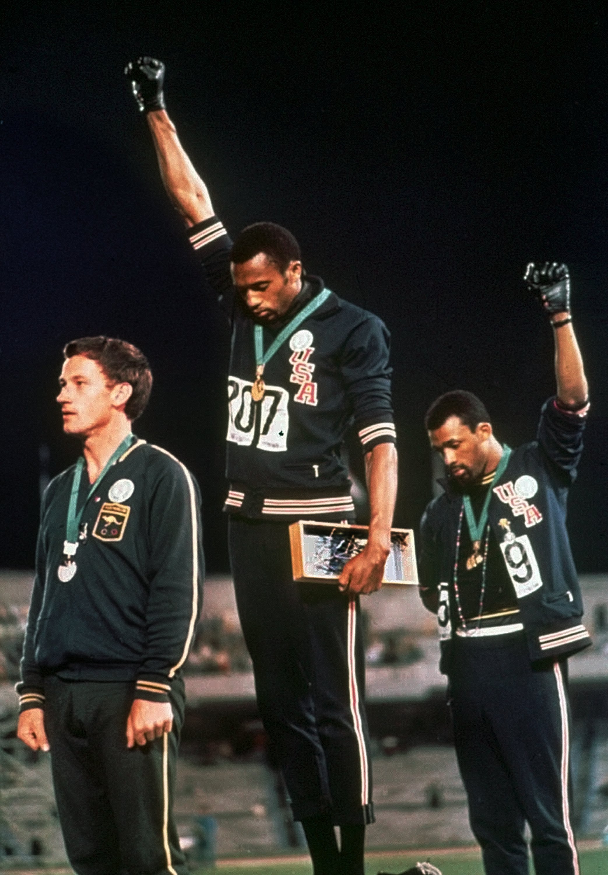 Extending gloved hands skyward in racial protest, US athletes Tommie Smith (centre) and John Carlos (right) stare downward during the 1968 Olympic medal ceremony [AP Photo]