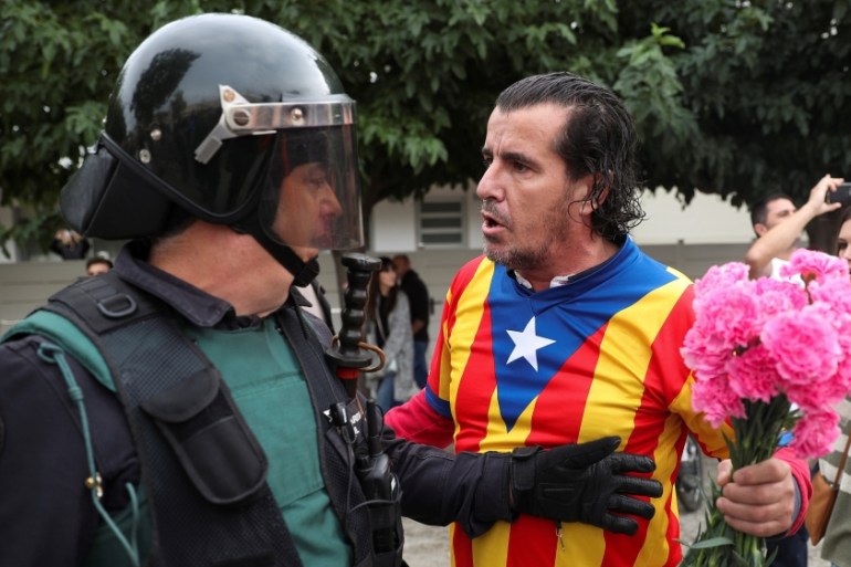 A man wearing a shirt with an Estelada (Catalan separatist flag) and holding carnations faces off with a Spanish Civil Guard officer outside a polling station for the banned independence referendum