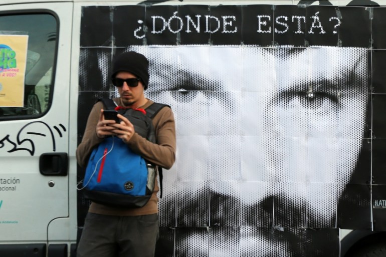 A man looks at his cell phone in front of a portrait of Santiago Maldonado at a demonstration to demand actions to find him, in Buenos Aires
