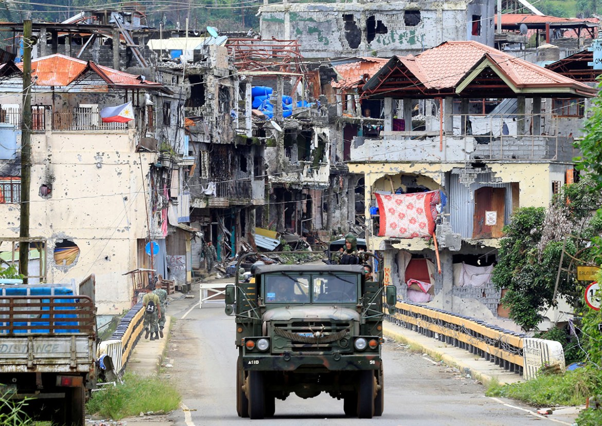 Soldiers on a military truck drive past houses and buildings damaged after government troops cleared the area from pro-Islamic State militant groups inside the war-torn Marawi city, southern Philippin