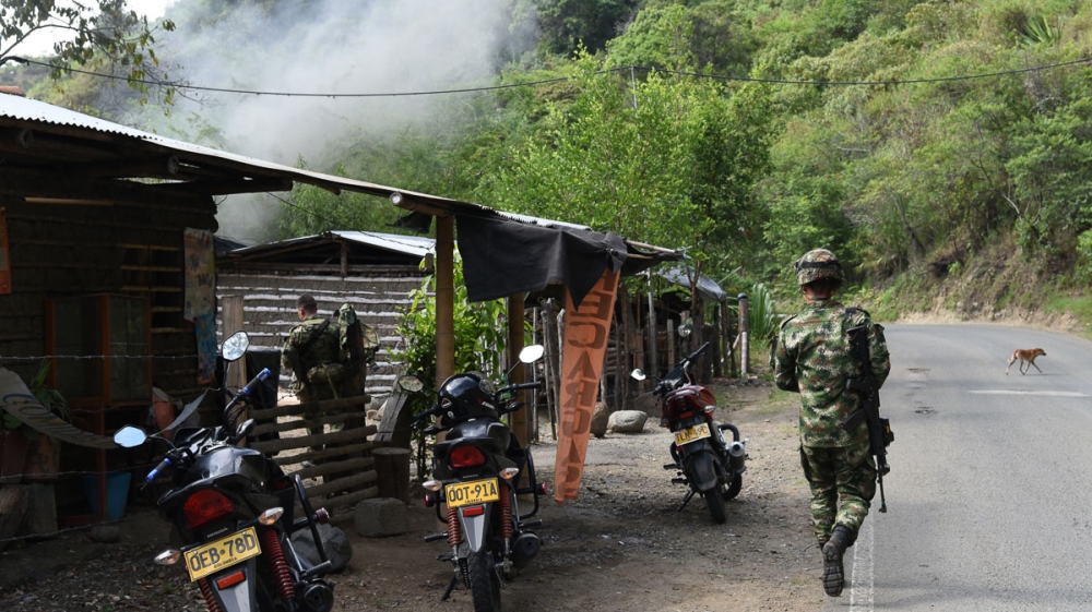 A soldier walks in front of the smoke produced by controlled explosions in an army operation to deactivate two bombs that were placed near a dam at a water treatment plant between El Palo and Toribio [Christian EscobarMora/Mira-V/Al Jazeera]