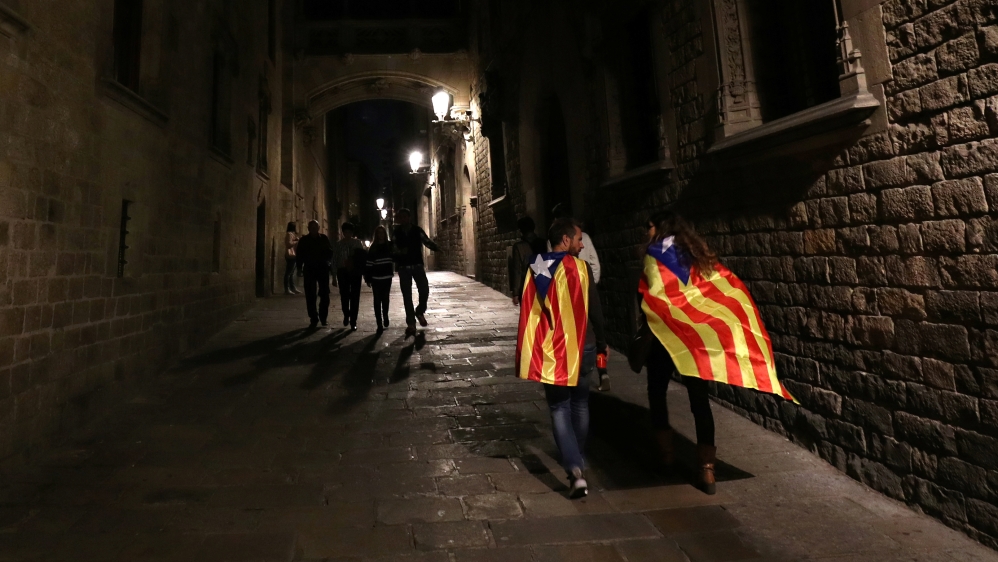 A couple wearing Esteladas (Catalan Separatist flag) walk down a street as they leave a protest in support of the members of the dismissed Catalan cabinet [File: Albert Gea/Reuters]