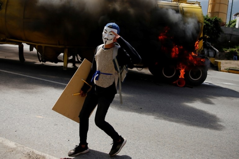 Demonstrator wears a Guy Fawkes mask next to a truck set on fire on a highway during a rally against Venezuela''s President Nicolas Maduro''s Government in Caracas