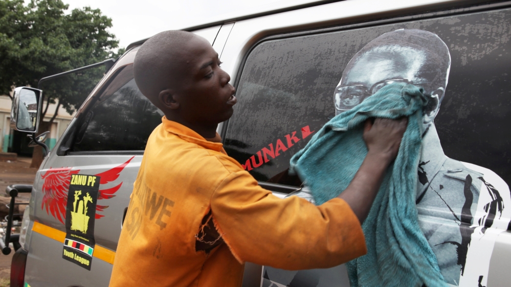 A young man washes a minibus adorned with picture of President Robert Mugabe at a bus terminus in Harare [Philimon Bulawayo/Reuters]