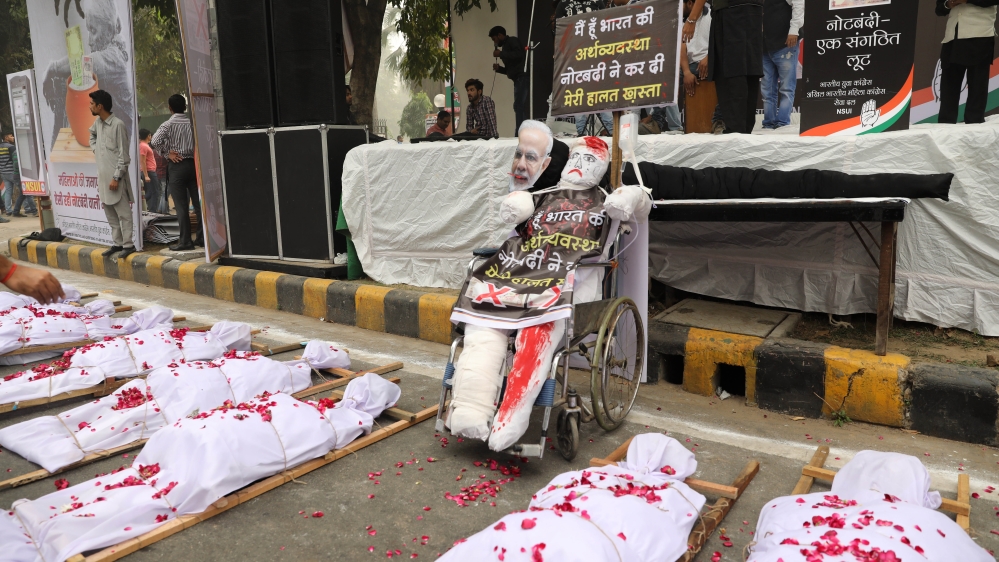 
Effigies depicting a wounded Indian economy is placed on a wheelchair next to mock bodies of people who allegedly died while standing in queues outside banks and automated teller machines (ATM) to withdraw money after the Nov. 8, 2016 demonetization, during a protest on the first anniversary of the demonetization announcement, in New Delhi, India [Supreet Jayanna/Al Jazeera]
