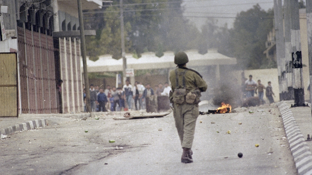 Two Israeli soldiers run towards a group of Palestinian youth, who had been hurling rocks and bottles at them in Nablus during the first intifada [AP/Max Nash]