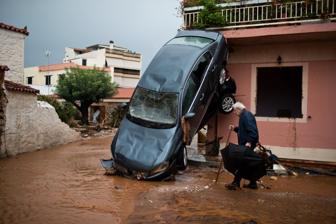 A man walks past a car moved by the force of flood water and a damaged house in the town of Mandra western Athens, on Thursday, Nov. 16, 2017. Greece''s fire department says rescue crews are searching