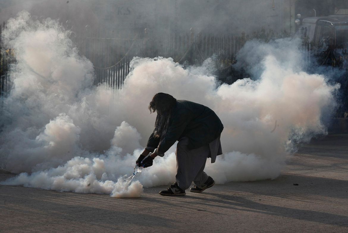 A protester pours water on a tear gas shell fired by police during a clash in Islamabad, Pakistan, Saturday, Nov. 25, 2017. Pakistani police have launched an operation to clear an intersection linking
