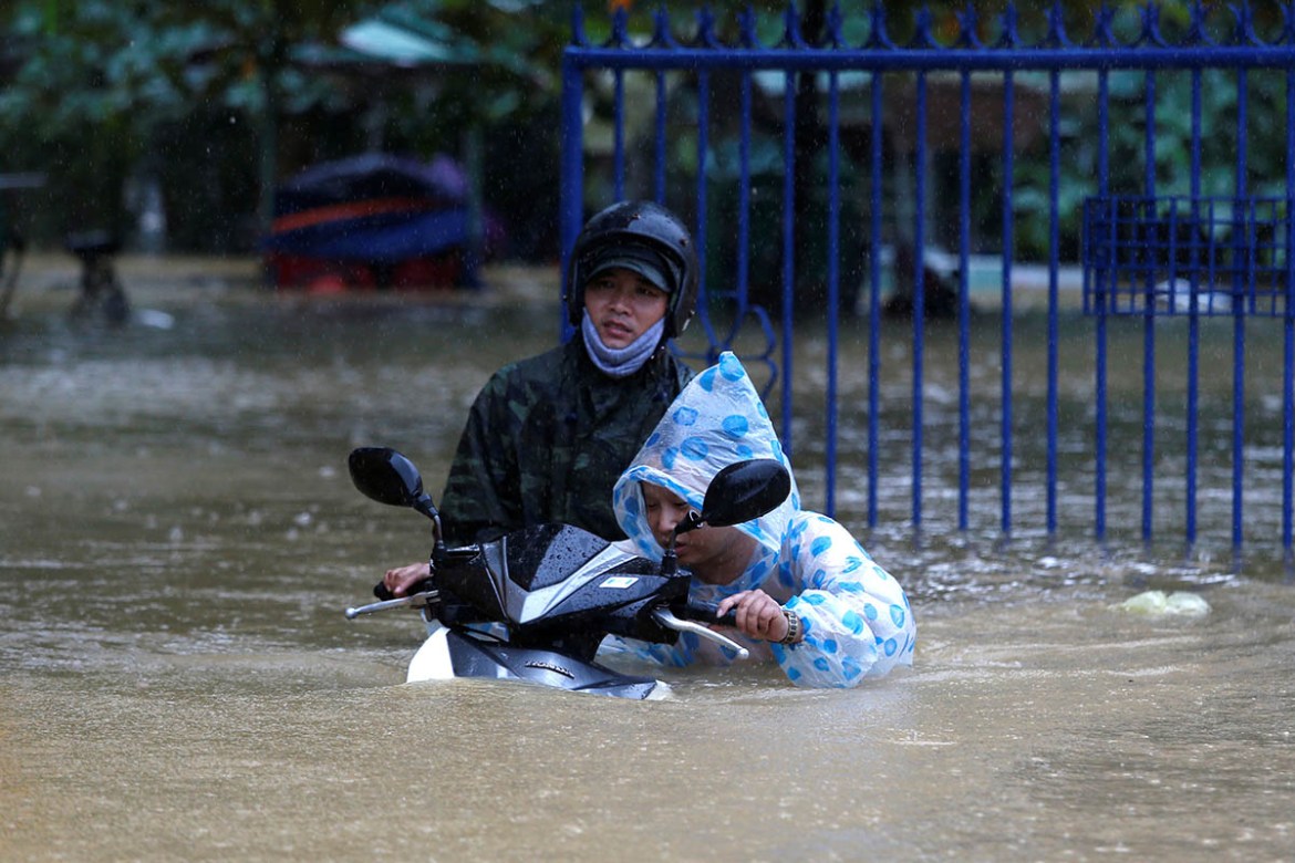 A woman pushes a motorbike along a flooded street in Hoi An. REUTERS/Kham