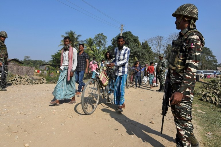 Villagers walk past CRPF personnel patrolling a road ahead of the publication of the first draft of the National Register of Citizens in the Juria village of Nagaon district
