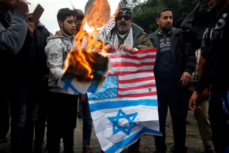 Palestinians burn signs depicting an Israeli flag and a U.S. flag during a protest against the U.S. intention to move its embassy to Jerusalem and to recognize the city of Jerusalem as the capital o