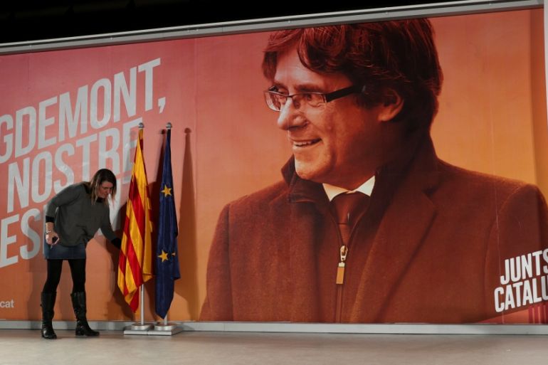 A woman arranges flags in front of a backdrop of ousted Catalan President Carles Puigdemont before a press conference by former Catalan cabinet members Jordi Turull and Josep Rull who were released