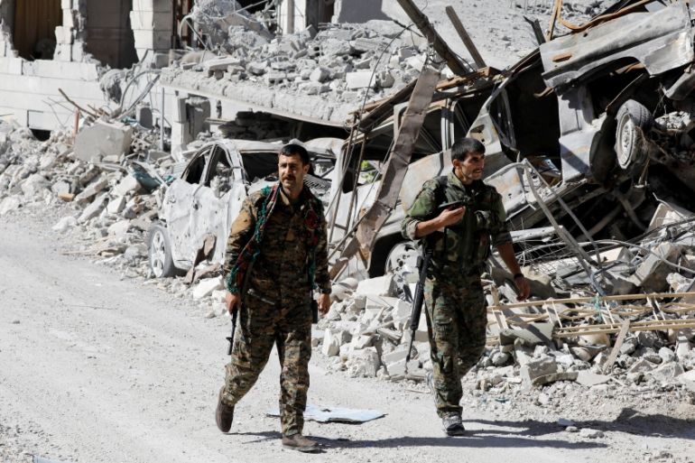 Fighters of Syrian Democratic Forces walk along a road past destroyed vehicles at the frontline in Raqqa