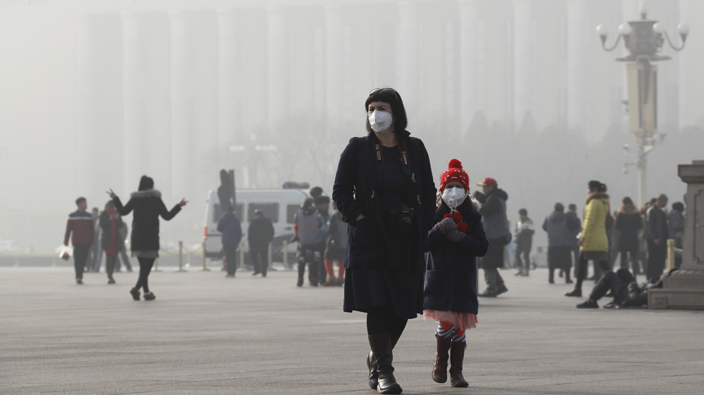 A foreign tourist and a child wearing protection masks walk through Tiananmen Square in Beijing [File: Andy Wong/AP]