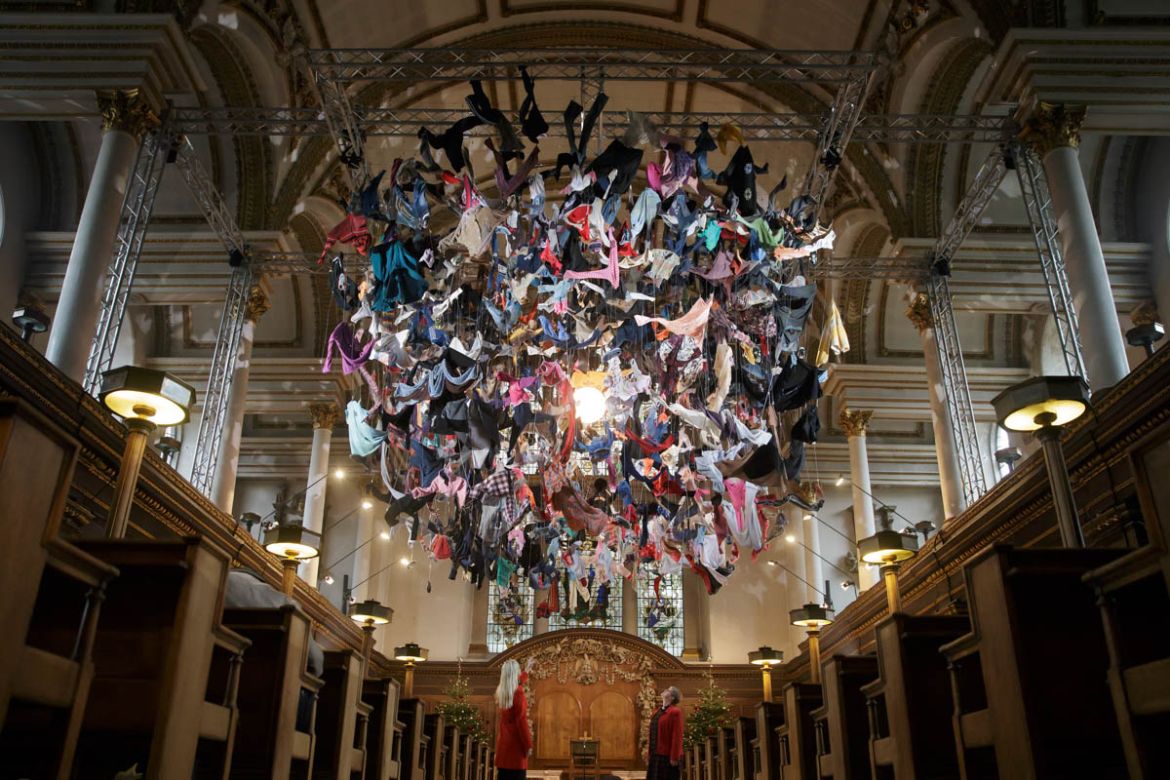 People pose for a picture to view an installation artwork called Suspended, composed of items of clothing discarded by refugees on their arrival at Lesvos, by artist Arabella Dorman, at St James''s Chu